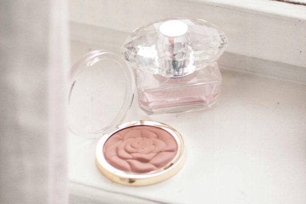 A delicate perfume bottle and blush in a rose pattern on an elegant windowsill create a vintage and chic atmosphere.