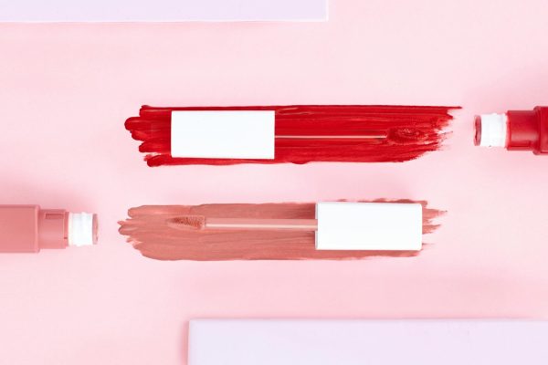 Top view of artistic makeup flatlay showcasing smeared lip gloss on a pink background.