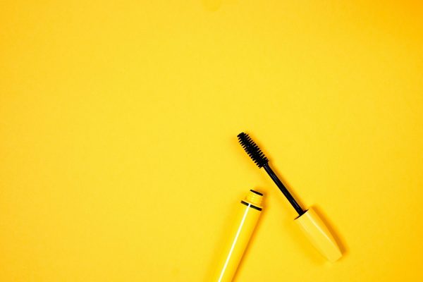 Open mascara with brush on vibrant yellow background, perfect for beauty and cosmetic themes.