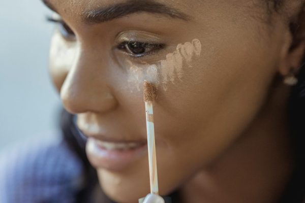 Close-up of a young woman applying concealer, highlighting her skincare routine for a flawless complexion.